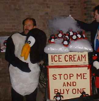 A man in a penguine outfit beside an exhibit, which is decorated with small toy penguins